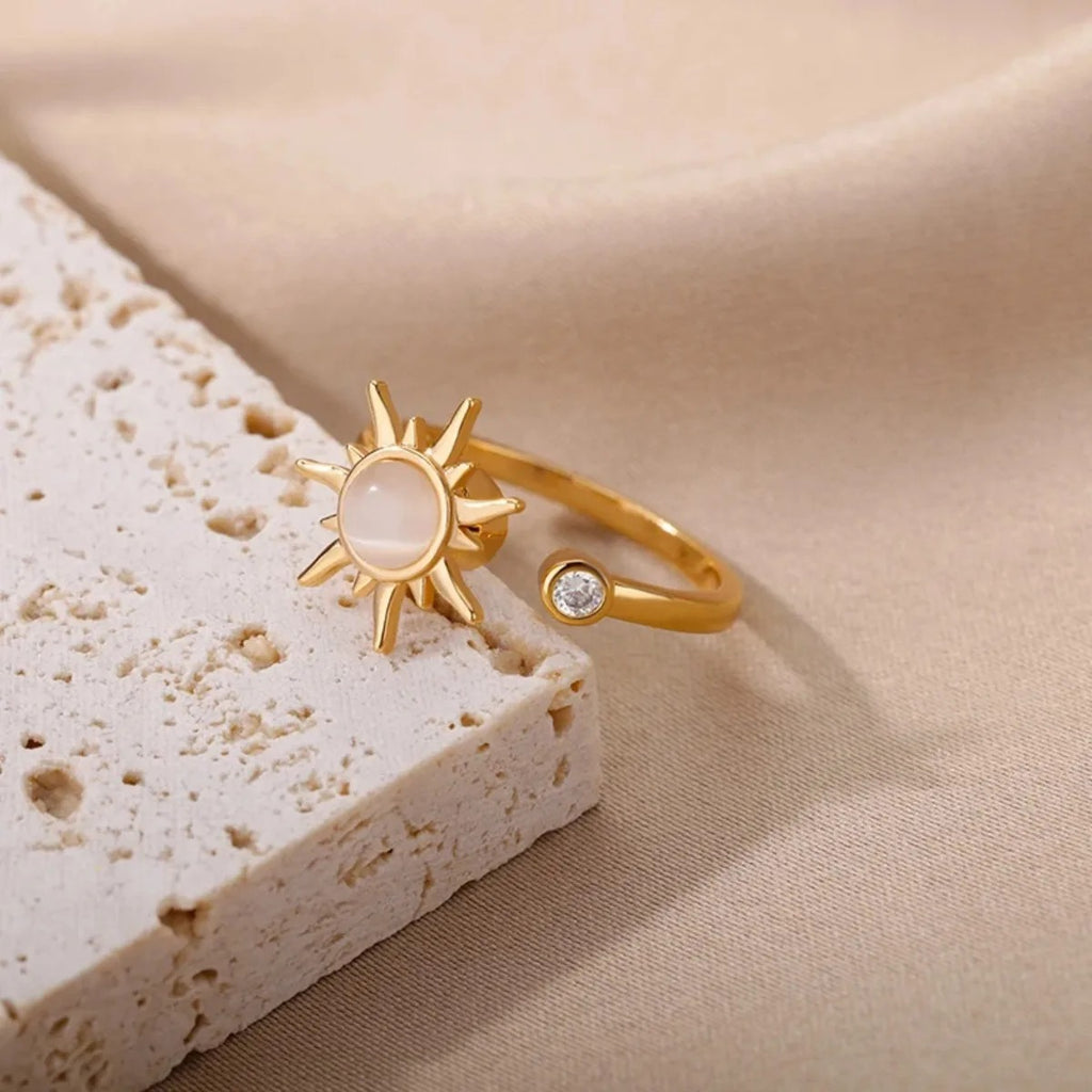 Gold ring with sun design on a beige stone surface
